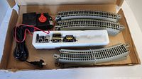 View of the train set components including controller, train cars in foam insert and curved tracks in the cardboard box
