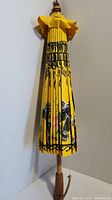 Closed yellow folding umbrella with black design and wooden handle leaning against wall.