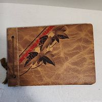 Photo of the brown leather-bound cover of the photo album with a leaf design and string binding.