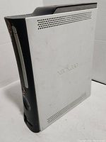 White and black Xbox 360 console with visible wear, showing side and front view with sticker residue and scuffs.