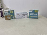 Three boxes of children safety locks including two boxes of 4our Kiddies Magnetic Cabinet Locks (12 locks + 2 keys each) and one box of Sunny Child Safety Locks (12 pack). Items appear new and unopened.