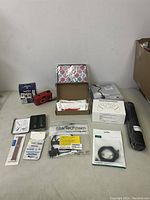 Overview of various items on table including watch bands, camera film, red compact camera, gaming controller box, microphone stand, cables, and colorful pouch.