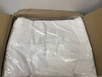 Photo of folded white sheet inside clear plastic packaging showing label with fiber content and product details.