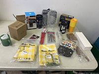 Full view of the lot showing various kitchen and home items on a table including towels, utensils, mugs, containers, and bags.