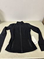 Full view of black Lululemon jacket laid flat showing front zipper, thumbholes, and sleek athletic design.