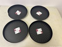 Four new Obsidian Gobel black round tart moulds with fluted edges and perforated bases arranged on a table.