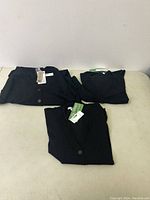 Three black cardigans folded together, showing tags and button details