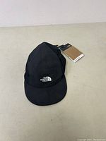 Black The North Face kids camp hat with curved brim and front embroidered logo, shown resting on a white surface.