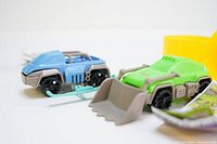 Close-up photo showing the blue snowmobile and green front-end loader toys from Kinder Surprise along with part of instruction leaflets and yellow egg capsules