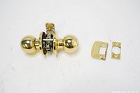 Polished brass spherical door knob set with latch mechanism and strike plates displayed on white background.