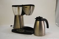 Front and side view of Kenmore model 80673 stainless steel coffee maker with detached stainless steel pot, power cord visible, on white background.