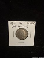 Front side of the 1910 UK silver one shilling coin showing the profile of King George V with inscriptions.