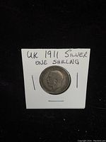 Obverse side of the 1911 UK silver one shilling coin showing King George V's profile and inscriptions, secured in a white holder with handwritten label.