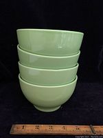 Stack of four lime green porcelain bowls against a black background with a ruler for size reference.