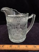 Side view of clear glass pitcher highlighting embossed birds, strawberries, and geometric patterned rim.