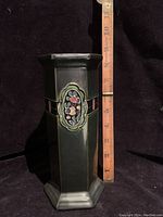 Full view of the vase with measuring tape beside it showing about 8.5 inches tall. Vase is hexagonal pillar shape, dark green, with gloss glaze.