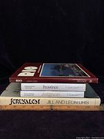 Top view of the four coffee table books stacked, showing the spines with titles and authors: 'Rio' by Aaron Cohen, 'Provence' by Graham Tabor and Franck B., 'Avignon' by Aaron Cohen, and 'Jerusalem' by Jill and Leon Uris.