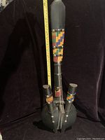 Front view of the gourd guitar showing the hollow body with black covering and colorful fabric wrapped wooden neck with four strings and tuning pegs.