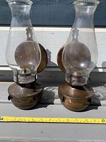 Pair of vintage copper/brass oil lamps with clear glass chimneys and measuring tape showing size.