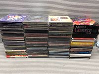 Stack of various random music CDs including compilations and artist albums, showing spines and some cover views.