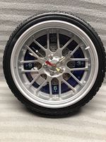 Front view of the tire clock showing black tire casing, silver rim, blue clock face with luminous green numbers and clock hands.