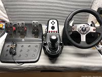 Full view of the Logitech G920 pedals, G27 shifter, and G25 steering wheel arranged on a cloth surface.