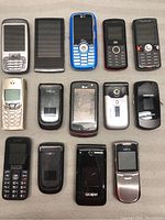 Grouped view of 14 older cell phones in candy bar and flip styles, various brands and colors mostly dark with some blue and silver, showing physical keypads and small screens.