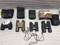 Four pairs of binoculars laid out with their carrying cases and original box for one pair.