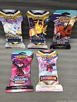 Five unopened Pokémon TCG booster packs displayed on a dark surface, showing the front artwork and seals.