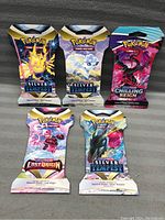 Five unopened Pokémon TCG booster packs laid out against a dark fabric background showing front packaging