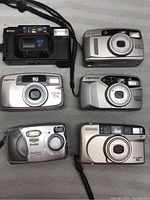 Six vintage film cameras arranged on a surface showing different brands and models.