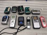 Full lot of 11 vintage and modern mini electronic devices arranged on table; includes MP3 players, digital recorders, USB flash drive, and other devices of varied designs and colors.