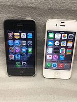 Front view of black and white first generation iPhones displaying apps screens, showing both are powered on and functioning.