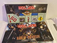 Two boxed Harley-Davidson branded Monopoly board games stacked, showing artwork featuring motorcycles and Harley-Davidson logos.