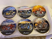 Six collectible Indian Motorcycle decorative plates displayed on fabric, each plate features a different vintage Indian motorcycle with gold trim and 'Indian' script.