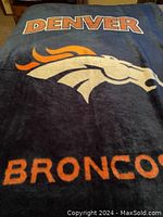 Denver Broncos twin-size blanket with large team logo and text displayed on bed.