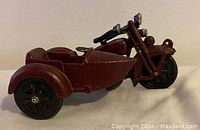 Side view of dark red cast iron motorcycle with sidecar showing paint wear and dirt.