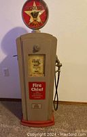 Front view of the vintage gas pump cabinet showing the beige body with red base, Fire Chief decal, display window and round illuminated Gasoline Service globe on top.