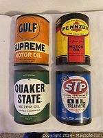 Top view close-up showing the vintage graphics and colors of four half metal oil cans: Gulf, Pennzoil, Quaker State, STP.