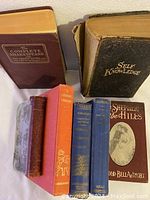 Full view of the book collection showing the spines and covers of seven vintage hardcover books arranged upright and stacked.