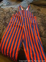 Full view of orange and blue vertically striped bib overalls laid flat.