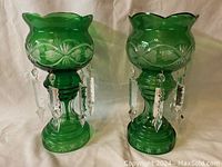 Pair of green glass mantle lusters with cut to clear design and hanging clear glass prisms in front view.