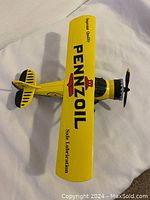 Top view of yellow Pennzoil diecast airplane bank showing logo and text on top wing and tail with propeller and cockpit details.