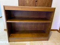 Wooden shelving unit with one adjustable shelf inside. Shows medium brown wood grain with visible wear.