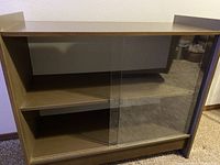 Front view of wooden cabinet with glass sliding doors showing two interior shelves and painted back side.