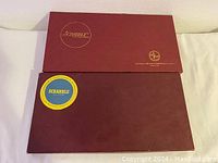 Two closed rectangular Scrabble game boxes with printed logos and branding.