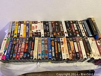 Two images showing a collection of various used VHS tapes arranged side by side. Titles visible include Goodfellas, Hollywood Knights, Kennedys, Rosewood, Legally Blonde, Beethoven 2, Office Space, Ghost, and several John Wayne films among others.