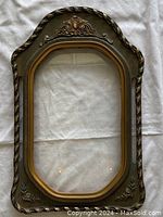 Front view of vintage wooden frame with ornate carvings and convex glass showing curled rope and floral details with gold inner border.