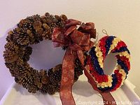 Pinecone wreath with red bow alongside patriotic flower wreath