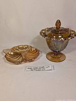 Both amber carnival depression glass items displayed together: the covered candy bowl with grape design and the divided candy dish